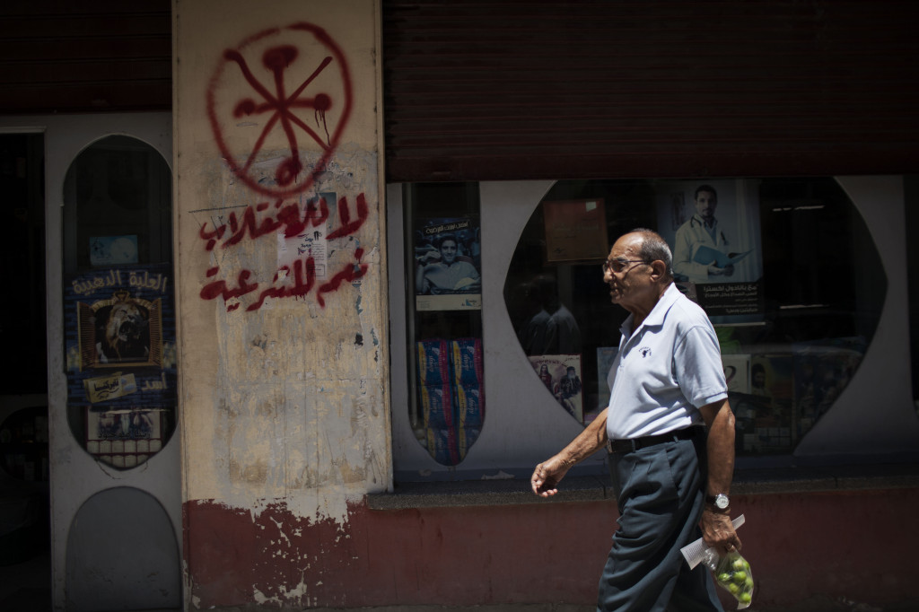 In this photograph from August 2013, an Egyptian man walks in front of a pharmacy marked with anti-Coptic and anti-coup graffiti in Assiut, Upper Egypt. Arabic graffiti reads, 